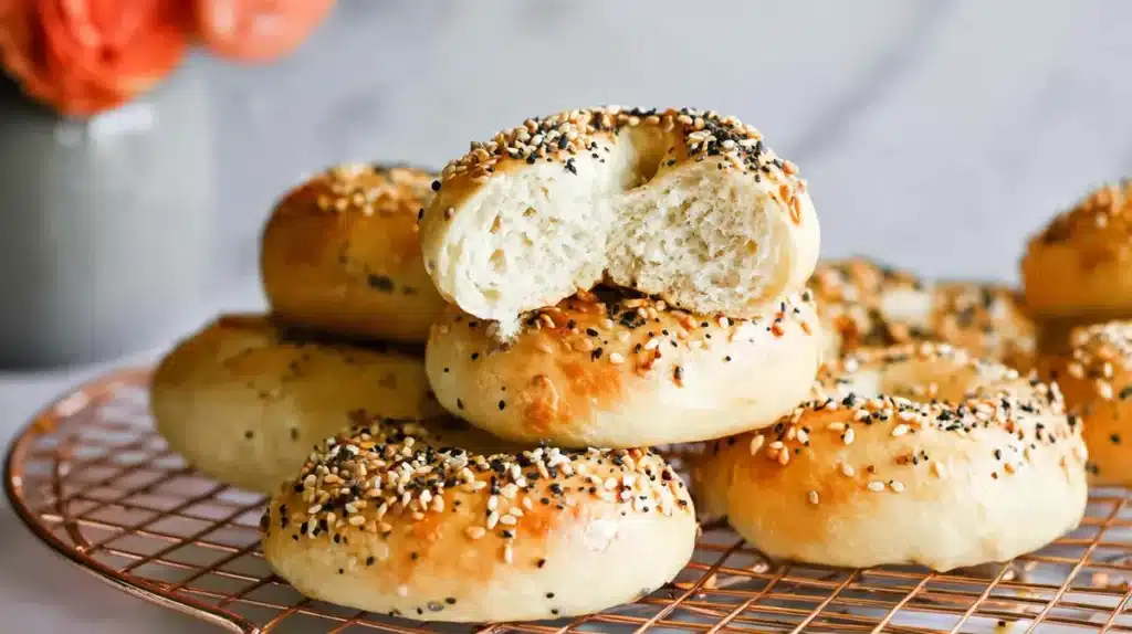 Protein Bagels Become Your Ultimate Obsession With 37g Of Pure Delight 5 High-protein bagels topped with seeds and spices arranged on a wire rack