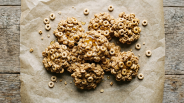 Overhead view of a cluster of golden no-bake cookies with Cheerios cooling on parchment paper with a honey drizzle.