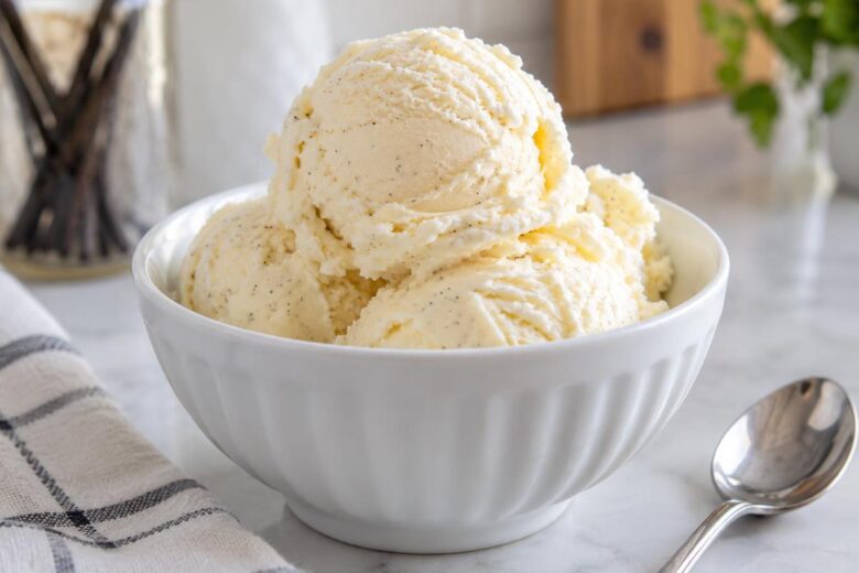 No Churn Ice Cream No Condensed Milk (Easy Vanilla Recipe) 16 Photo of No Churn Ice Cream No Condensed Milk (Easy Vanilla Recipe) (no churn ice cream no condensed milk): A close-up of creamy vanilla no churn ice cream no condensed milk scooped into a chilled white bowl, showing soft rounded scoops, tiny vanilla flecks, and a small silver spoon on a light kitchen counter