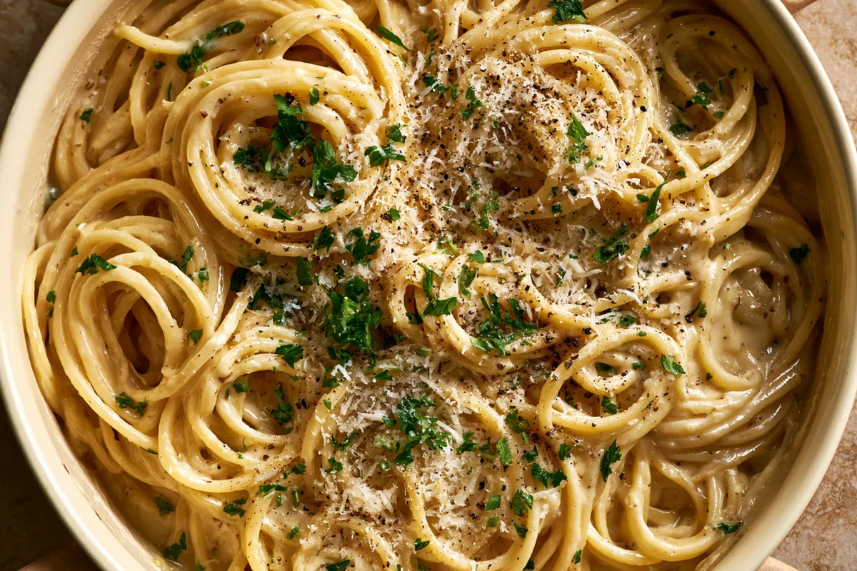 One Pot Creamy Garlic Pasta with Parmesan 1 Photo of One Pot Creamy Garlic Pasta with Parmesan (one pot creamy garlic pasta): A close overhead view of one pot creamy garlic pasta, glossy spaghetti coated in creamy Parmesan garlic sauce in a wide cream-colored skillet, topped with finely grated Parmesan, black pepper, and chopped parsley