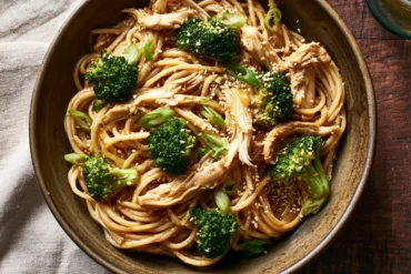 Photo of Pasta and Rotisserie Chicken Recipes: Sesame Ginger Noodles (pasta and rotisserie chicken recipes): A warm overhead serving bowl of sesame ginger spaghetti with shredded rotisserie chicken, bright green broccoli florets, sliced green onions, and sesame seeds, showing an easy pasta and rotisserie chicken recipe in a cozy home kitchen